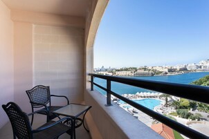 Varanda com mesa e cadeiras, com vista para um horizonte costeiro, piscina e praia.