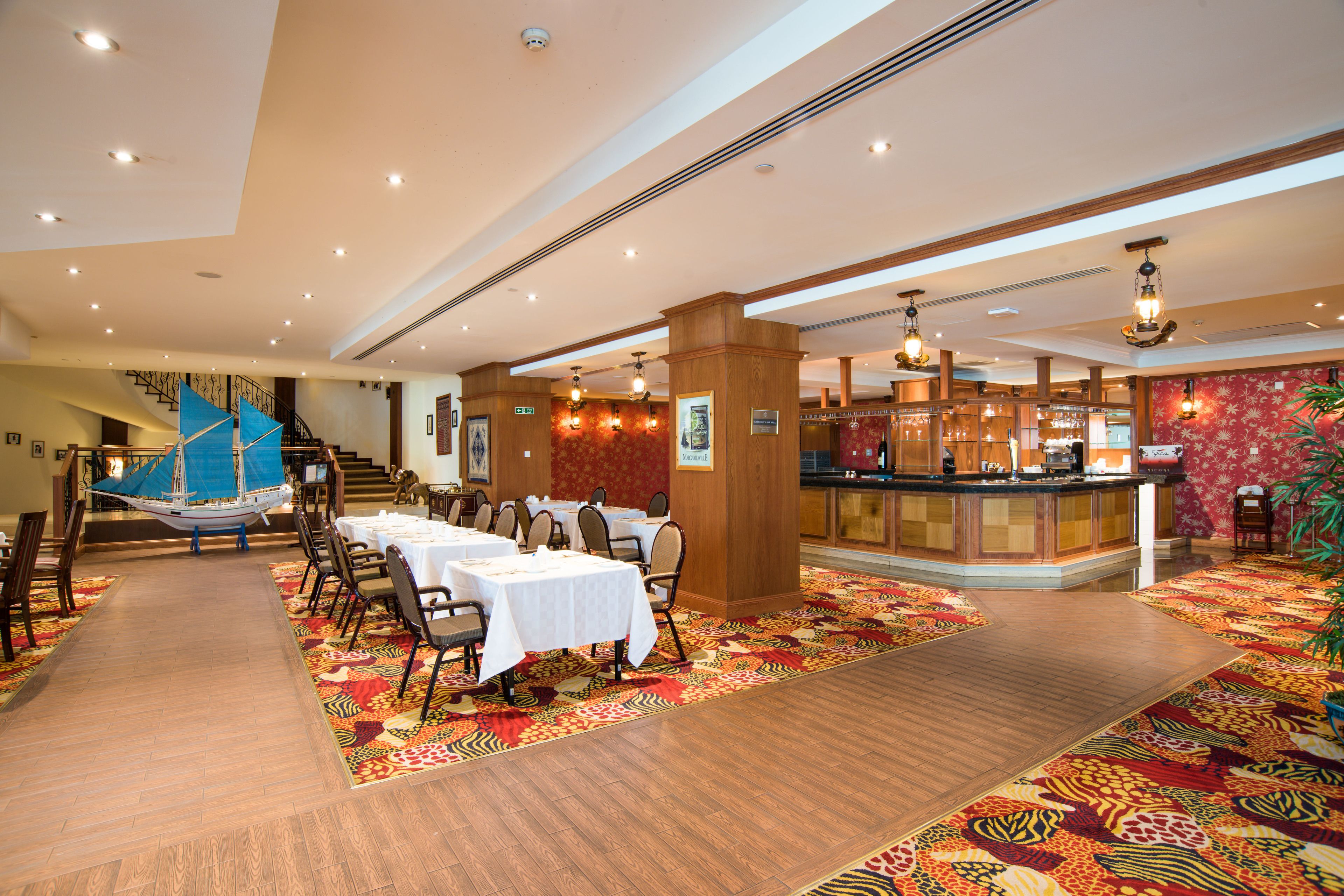 Un vaste espace dédié à la salle à manger, avec de nombreuses tables et chaises, un bar central et un escalier menant à un niveau supérieur.