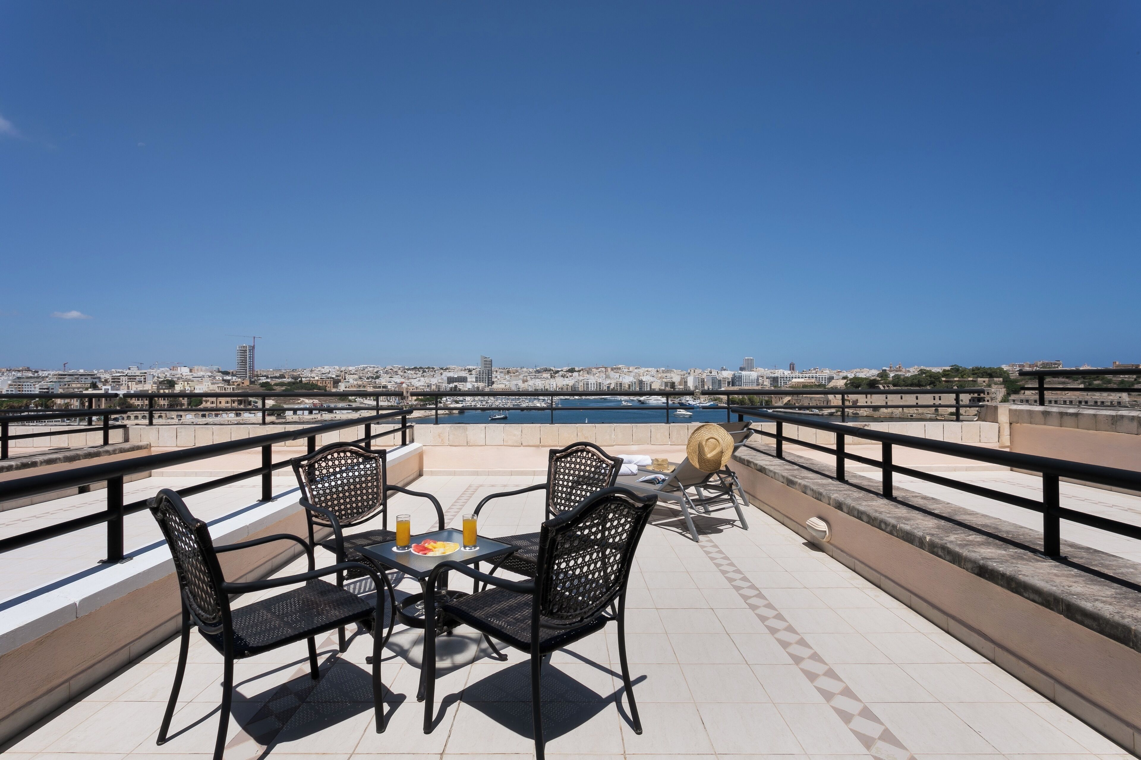 A terrace with a table and chairs, overlooking a marina and cityscape.