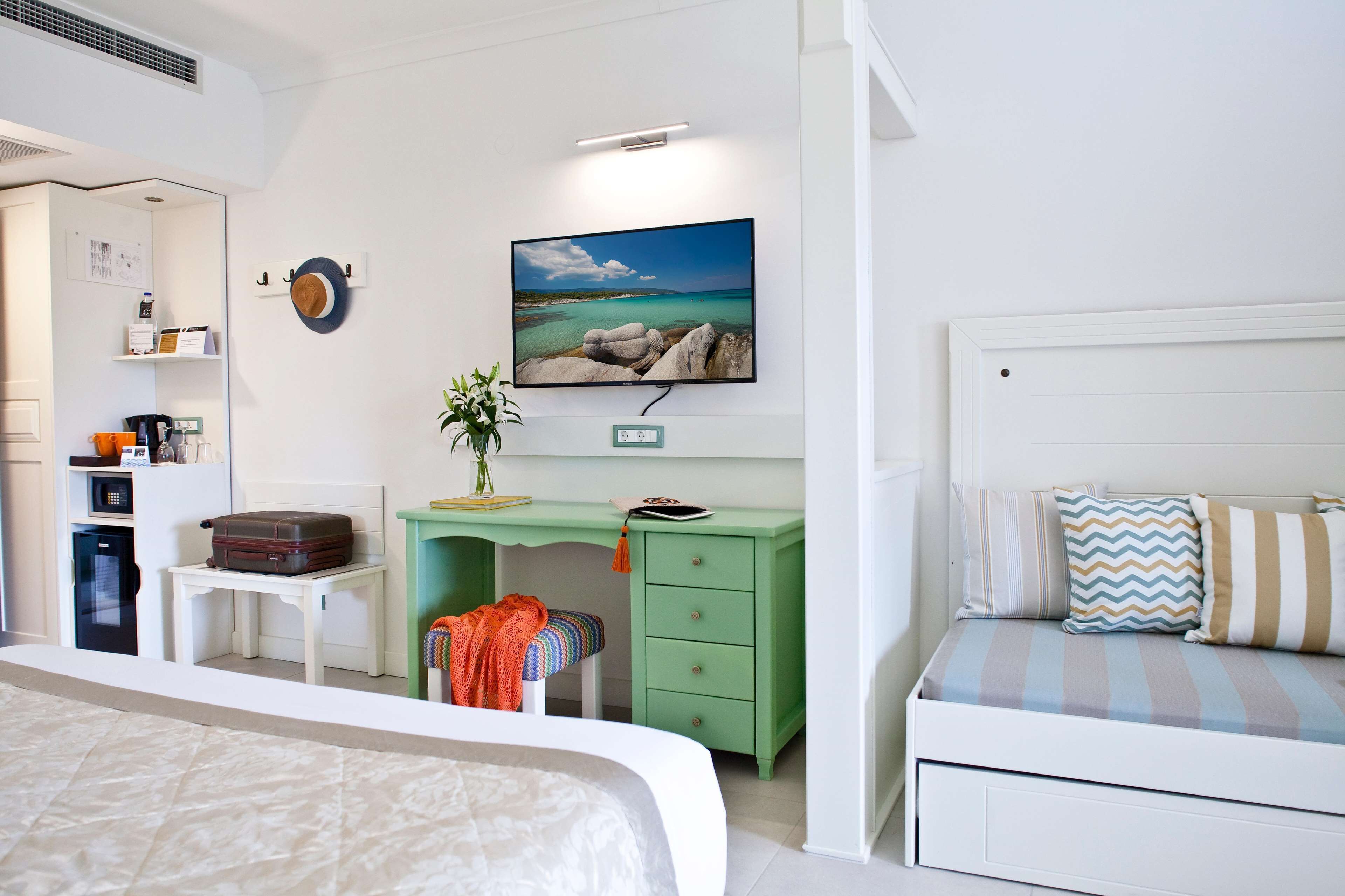 A bedroom with a bed, a desk with a computer, a chair, and a TV on the wall.