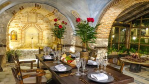 A dining area with a stone wall, a wooden table set for a meal, and a vase with red flowers. - Acrotel Athena Pallas & Residence (Sithonia)