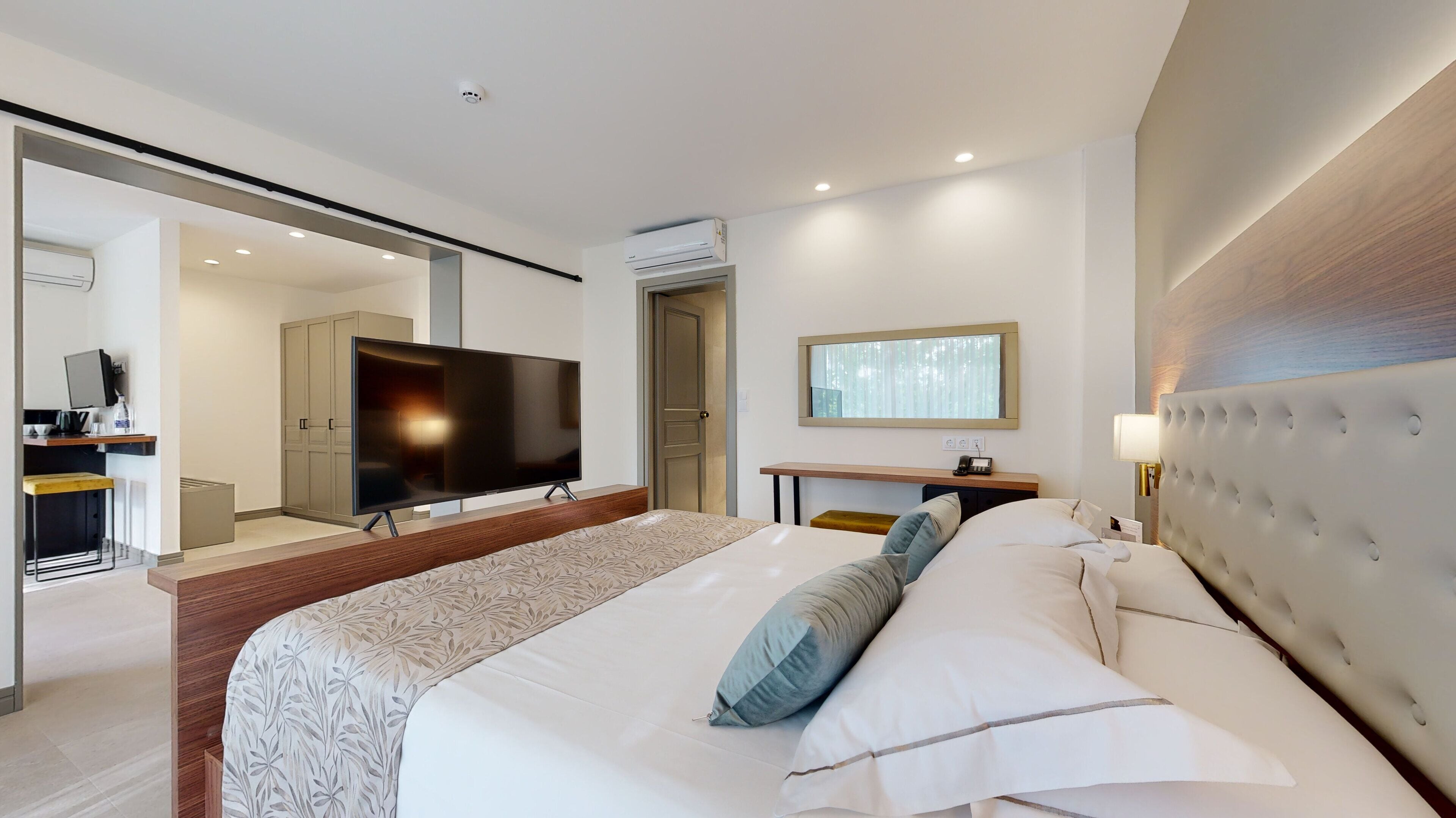 Una habitación de hotel moderna con una cama grande, un televisor de pantalla plana, un escritorio con una silla y un espejo.