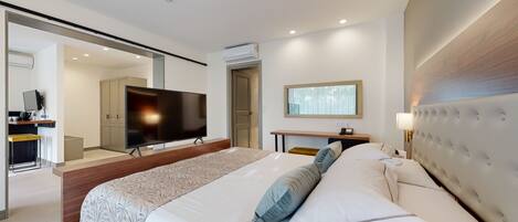 Una habitación de hotel moderna con una cama grande, un televisor de pantalla plana, un escritorio con una silla y un espejo.