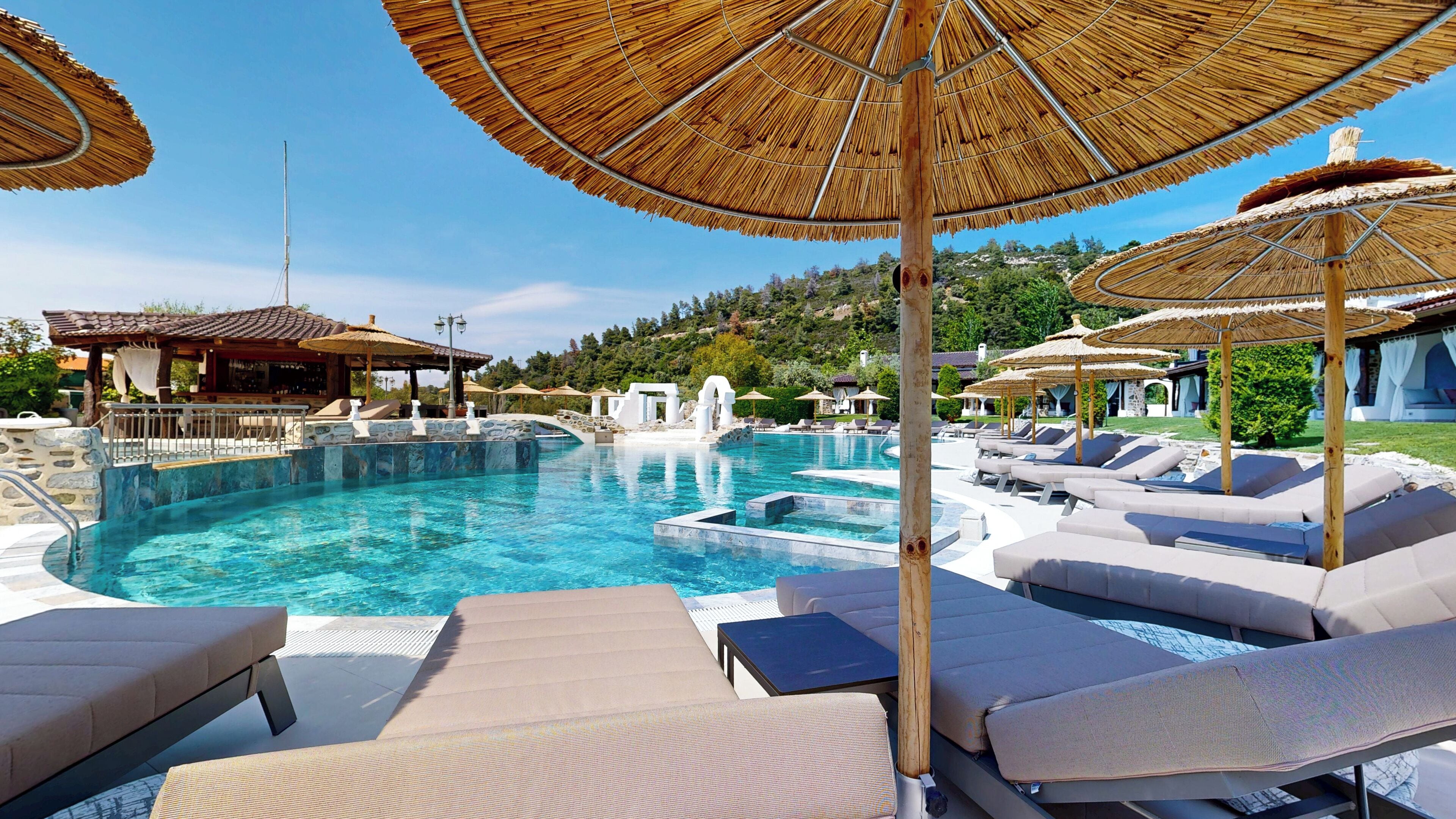 A pool area with lounge chairs and umbrellas, surrounded by a stone pool and a view of the hills.