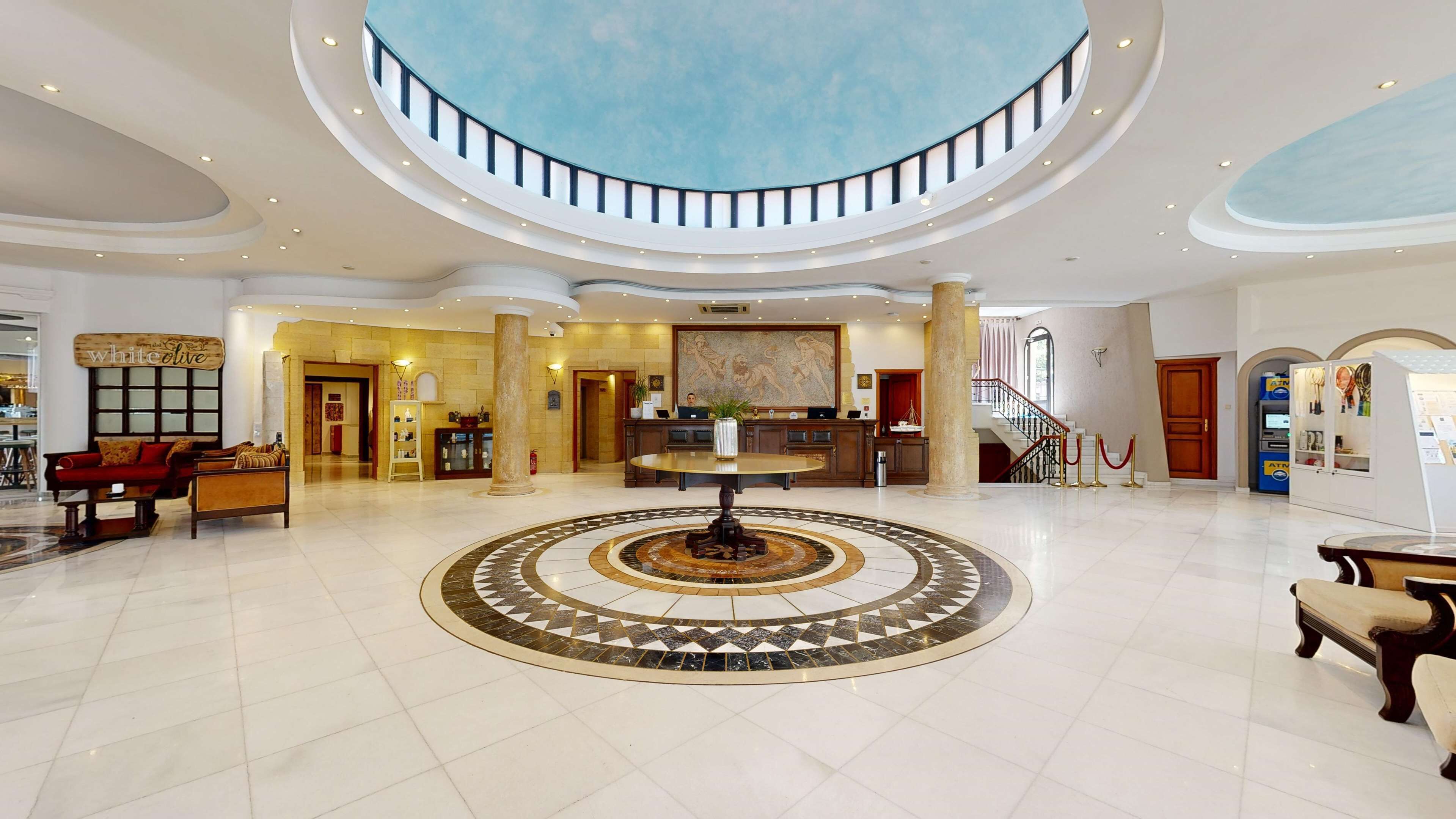 A spacious lobby with a central round table, a staircase, and a reception desk.