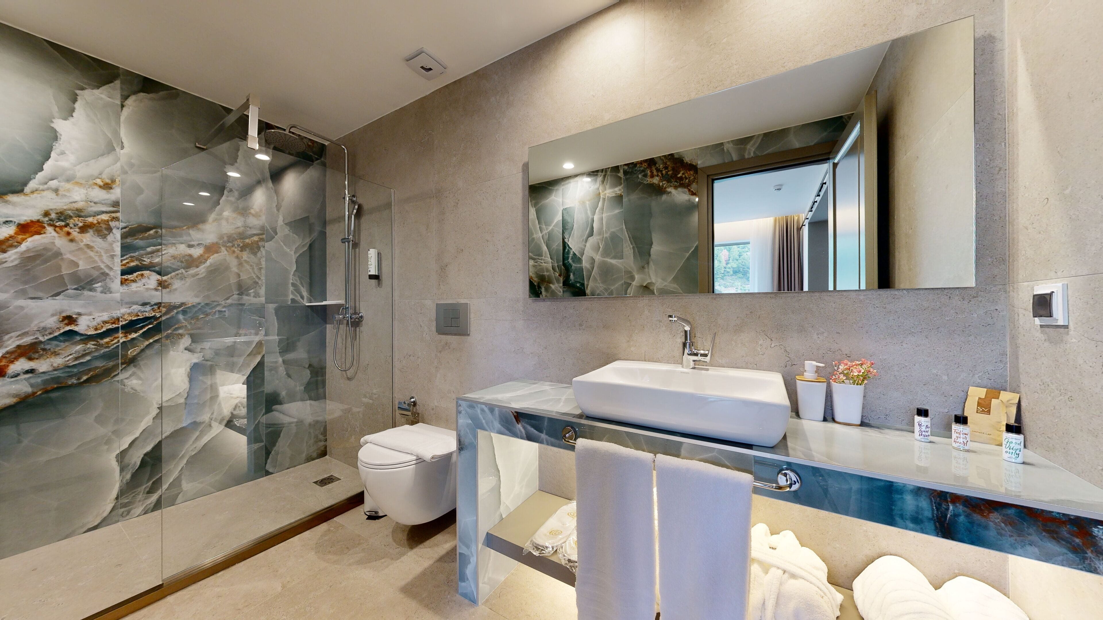 A modern bathroom with a marble shower wall, a glass-enclosed toilet, and a marble vanity with a sink.