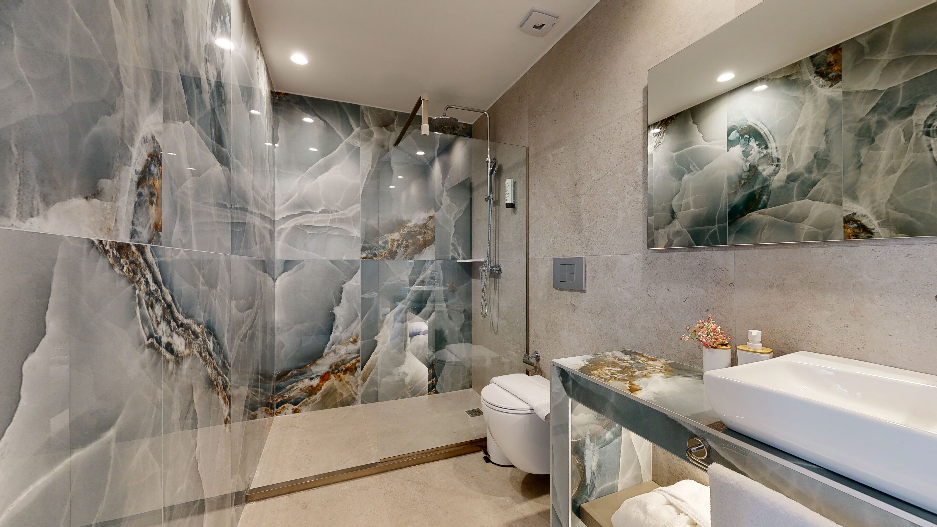 A modern bathroom with a glass shower enclosure, a white toilet, and a vanity with a marble countertop.