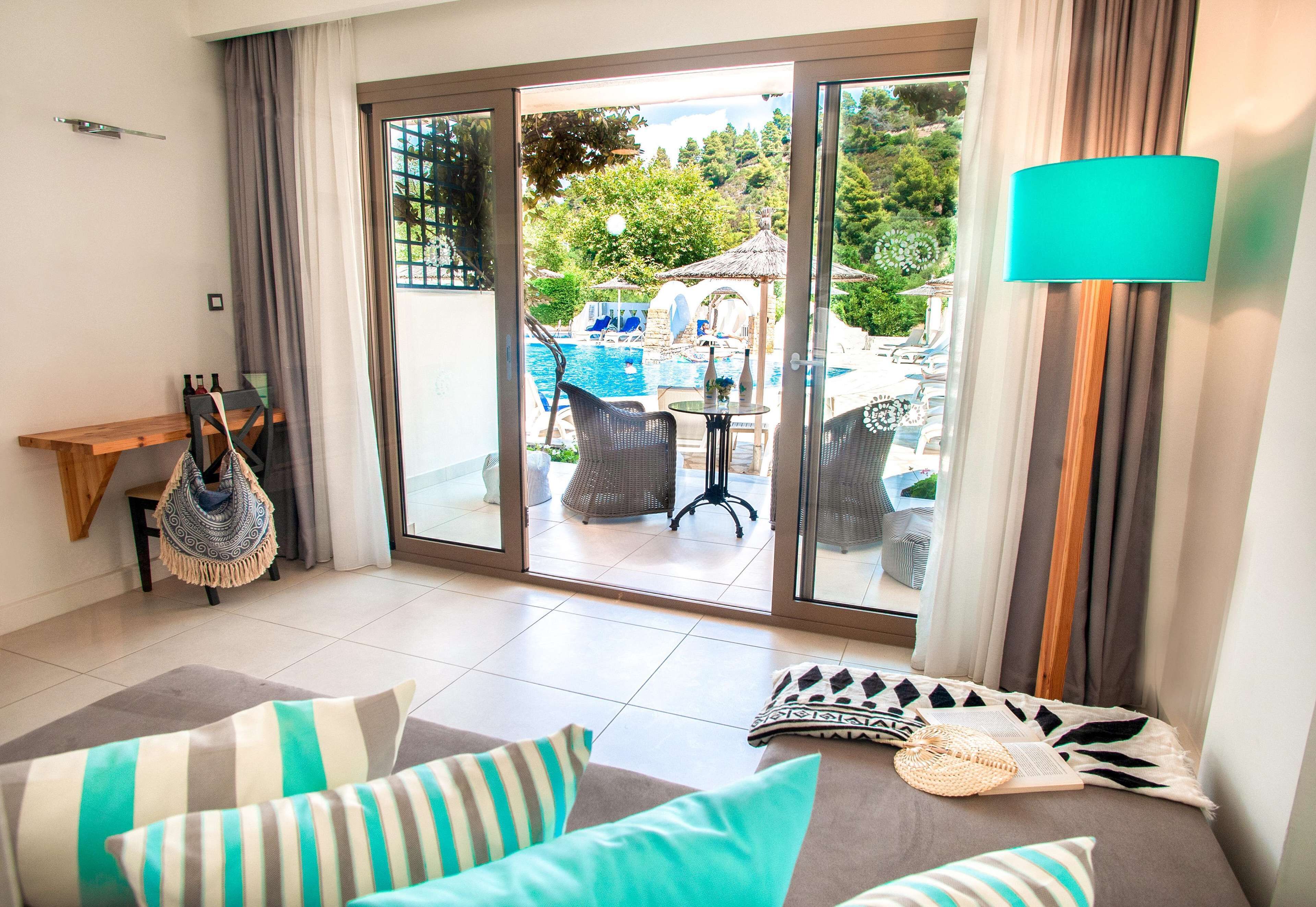 A room with a sofa, a small table, and a view of an outdoor swimming pool area.