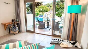 A room with a sofa, a small table, and a view of an outdoor swimming pool area.