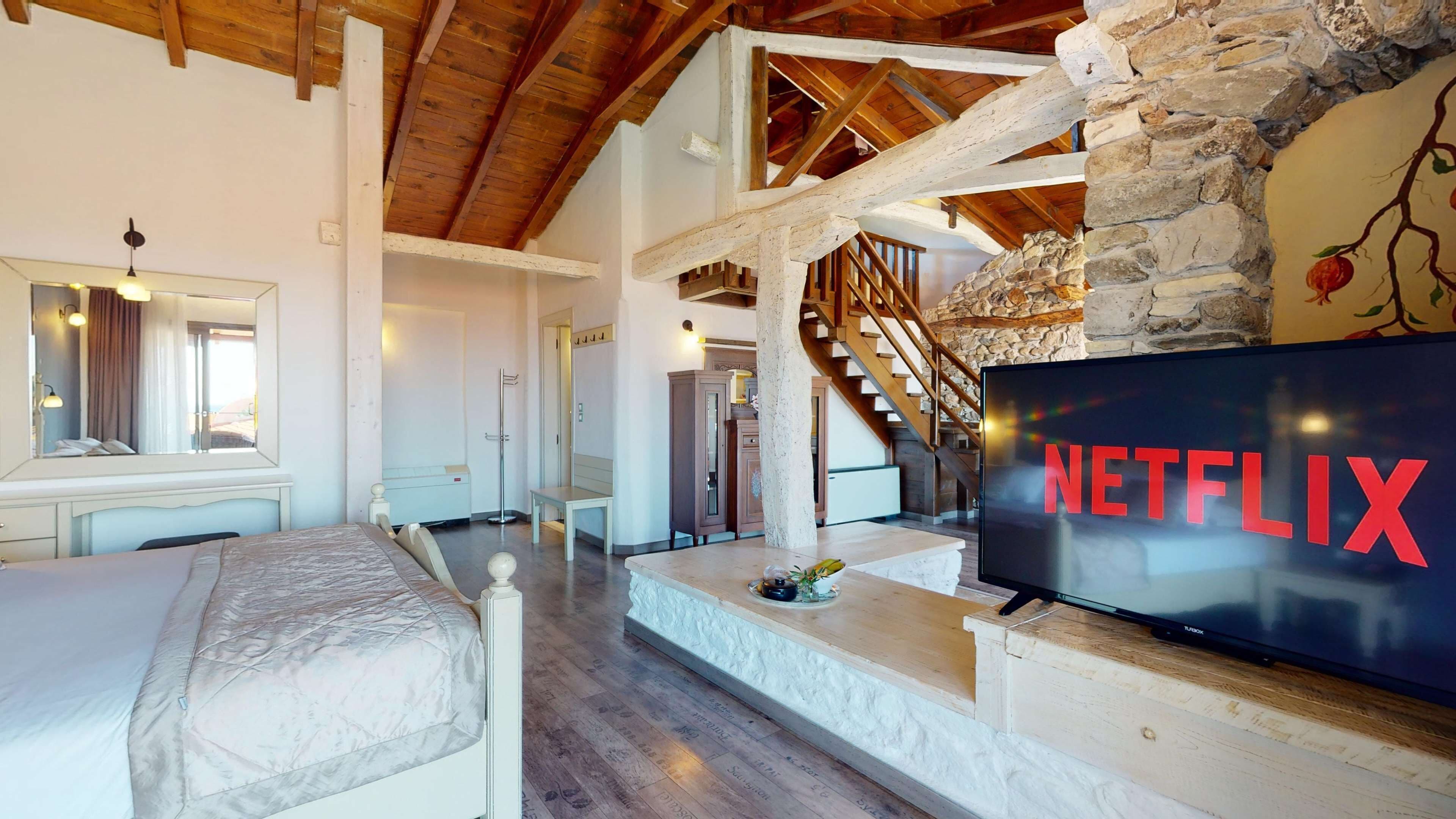 Ein modernes Hotelzimmer mit einem großen Bett, einem Fernseher mit Netflix-Logo, einer Steinwand und einer Holztreppe.