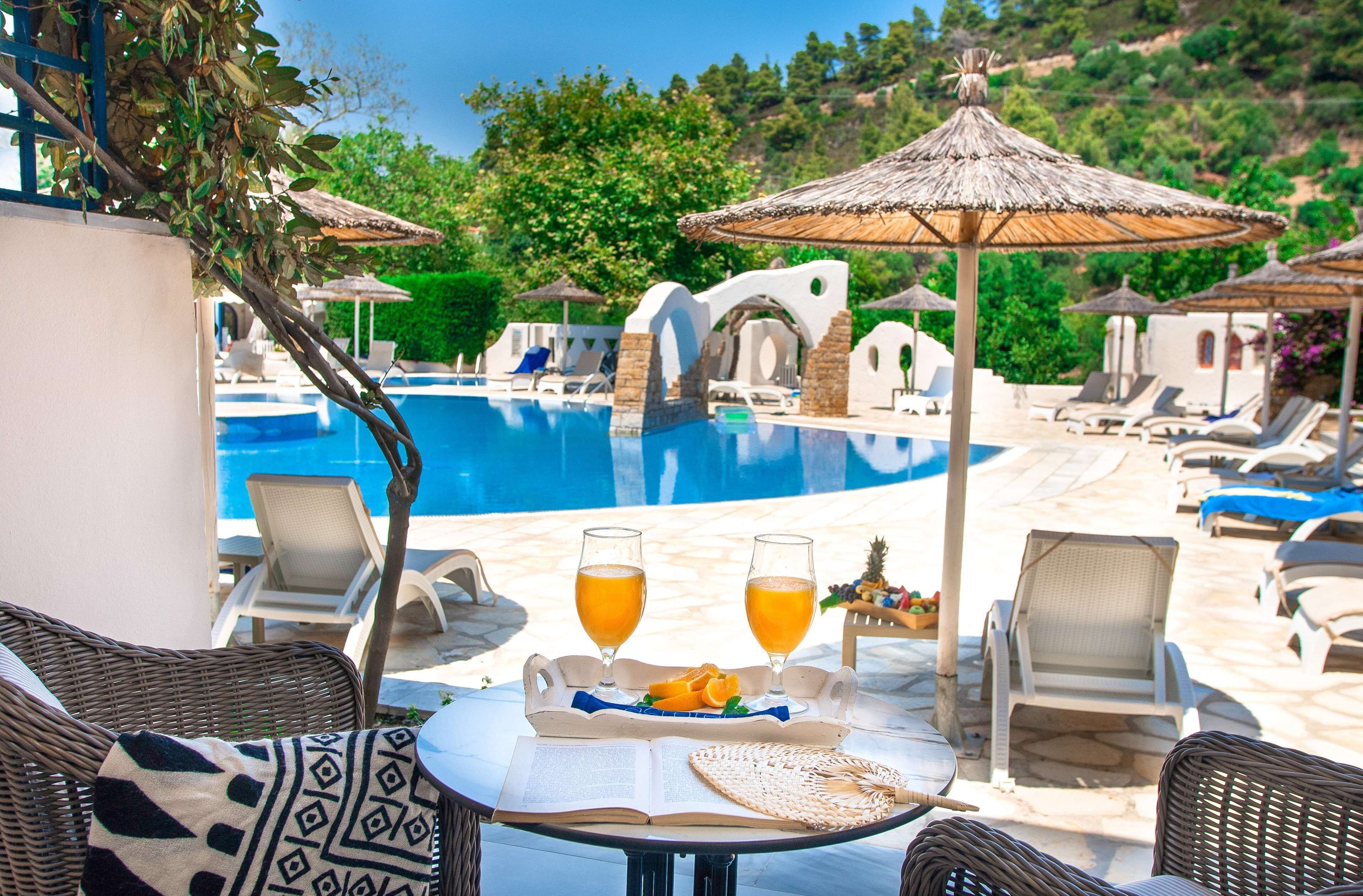 Ein Poolbereich mit Liegestühlen, Sonnenschirmen und einem Tisch mit Getränken und Obst.