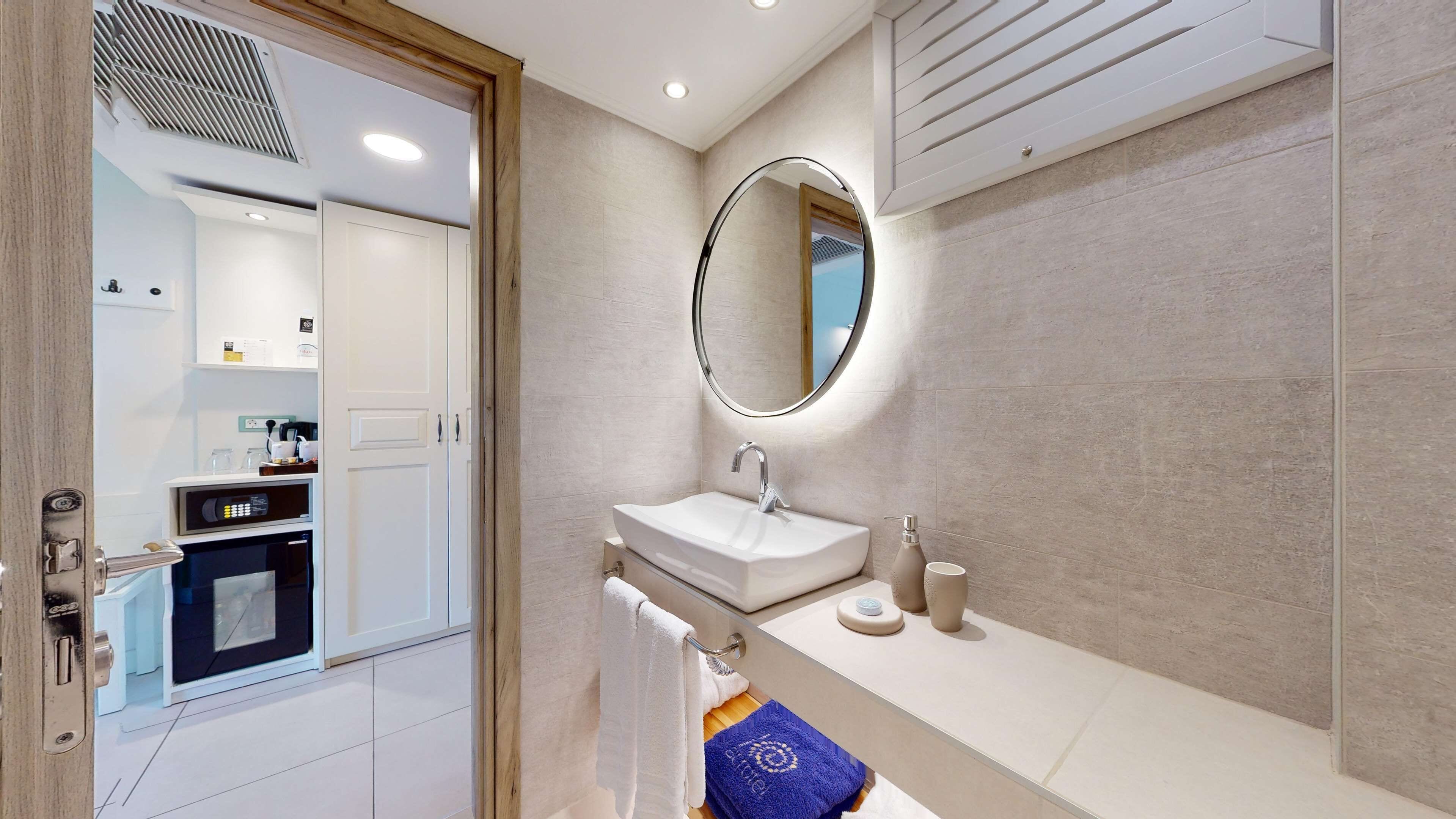 A modern bathroom with a white sink, a round mirror, and a towel rack.