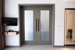 Una habitación moderna con una puerta gris, un televisor montado y un escritorio pequeño con teléfono.