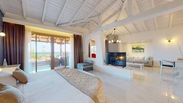 A spacious bedroom with a large bed, a balcony with curtains, a TV, and a seating area with a sofa and a coffee table.
