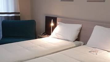 Una cama doble con ropa blanca, una mesita de noche con lámpara y cuadros enmarcados en la pared.