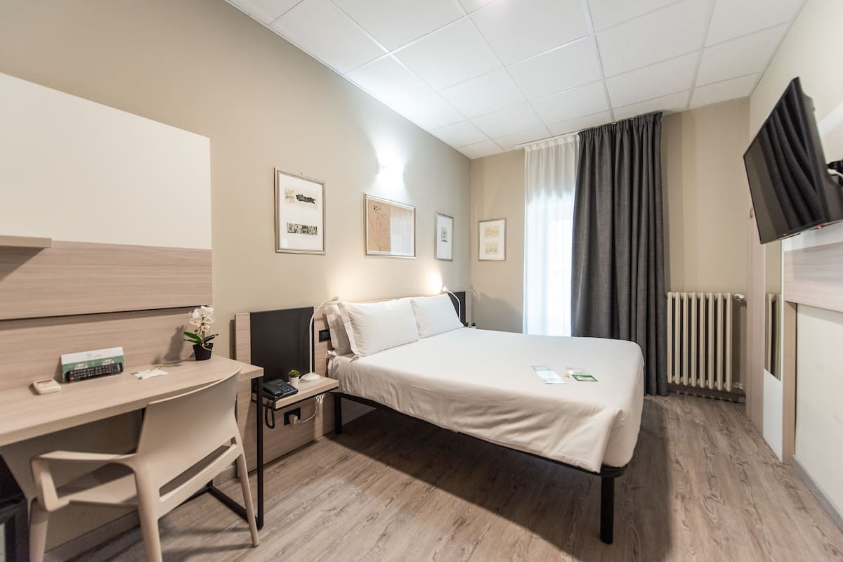 Ein Hotelzimmer mit Bett, Schreibtisch, Stuhl und Fernseher.
