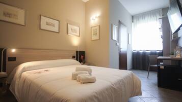 A hotel room with a large bed, a desk, a chair, and a television.
