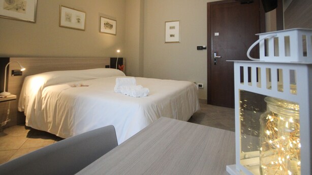 A hotel room with two beds, a desk, and a nightstand. There are framed pictures on the wall, a door, and a white cabinet with lights. - Hotel Gran Torino (Turin)