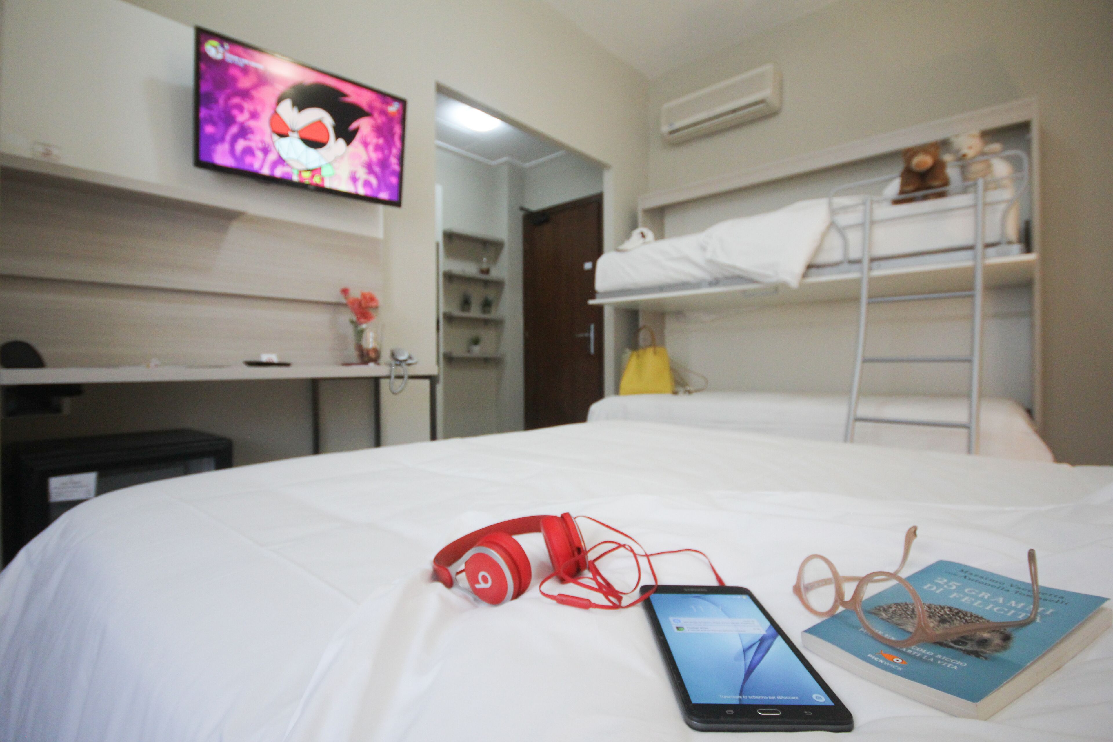 A hotel room with a bed, a desk, a TV, and a bunk bed.