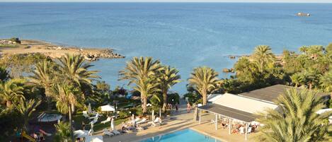 A pool area with lounge chairs and umbrellas, overlooking a beach and the sea.