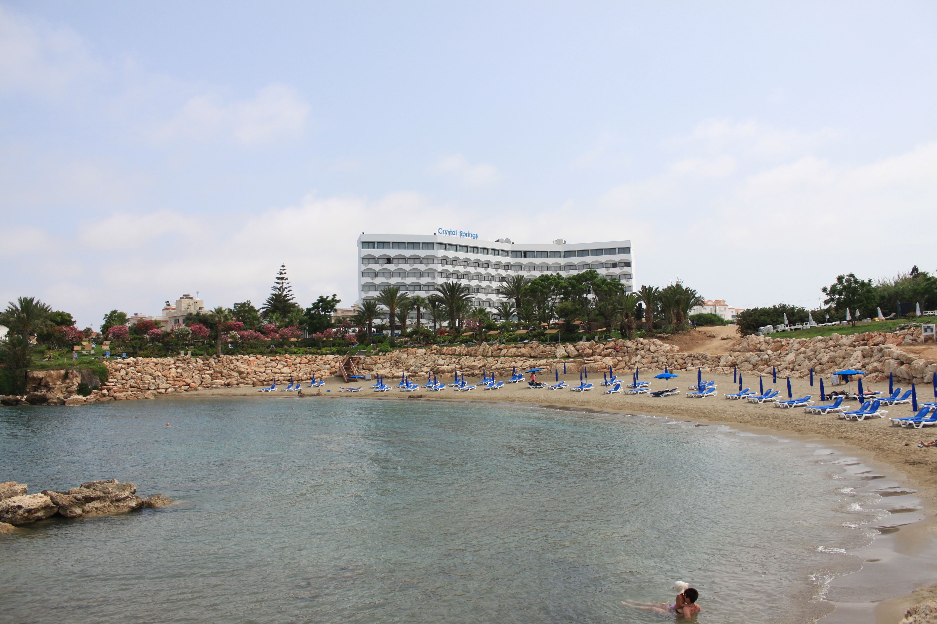 A beach with clear water, a hotel named "Crystal Springs" in the background, and several blue beach umbrellas.