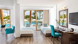 A hotel room with two beds, a desk, a TV, and a view of a pool and palm trees. - Crystal Springs Beach Hotel (Paralimni)