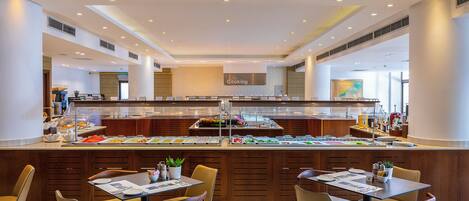 A buffet area with a variety of food options, a counter with a 'The Cooking' sign, and seating arrangements.