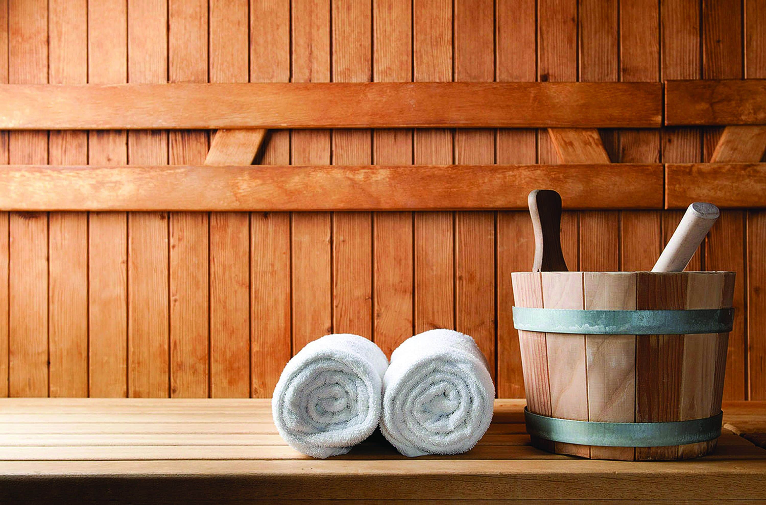 Two rolled towels and a wooden bucket with a brush on a wooden bench against a wooden wall.