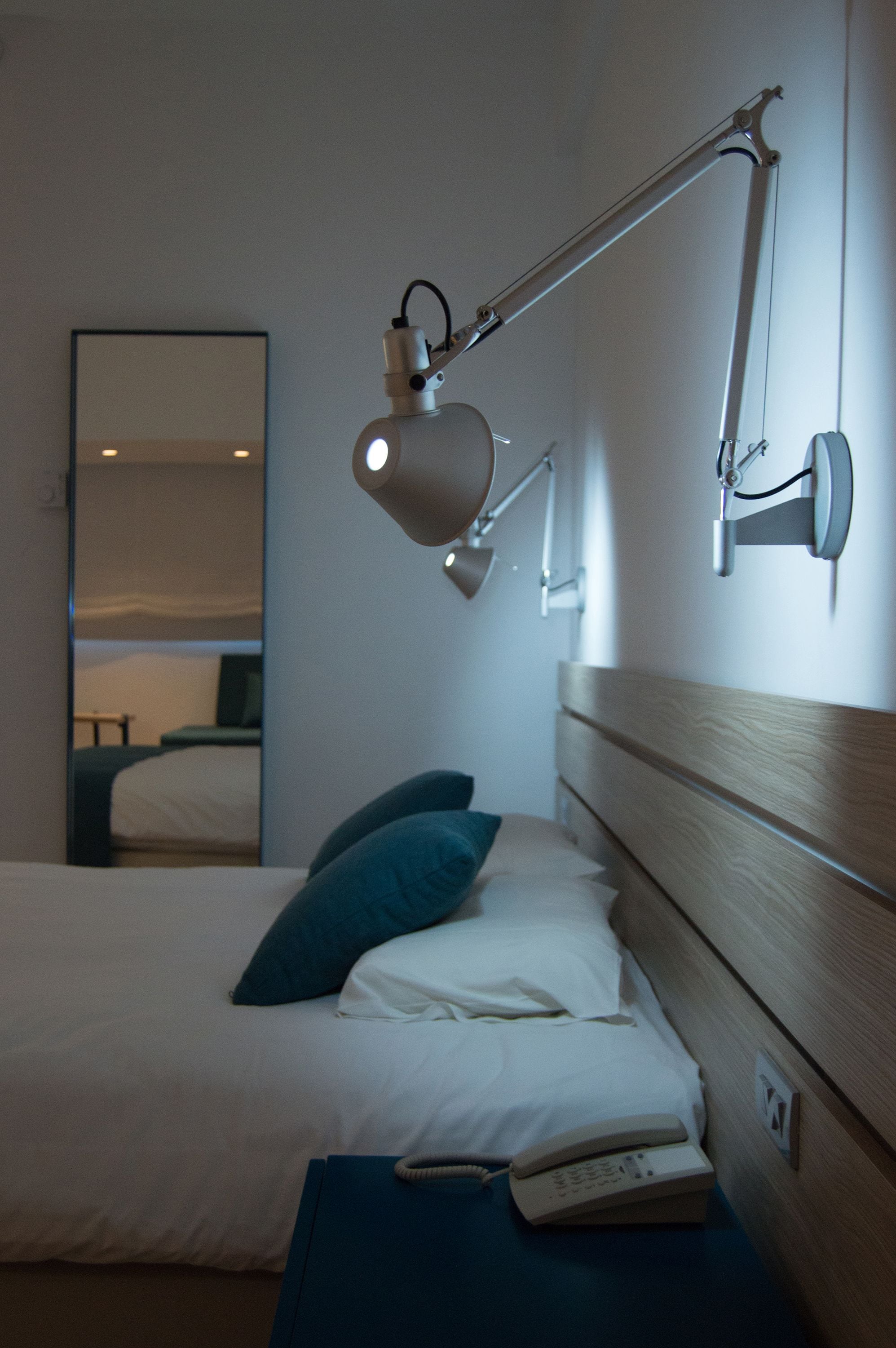A hotel room with a bed, a bedside lamp, a telephone, and a mirror on the wall.