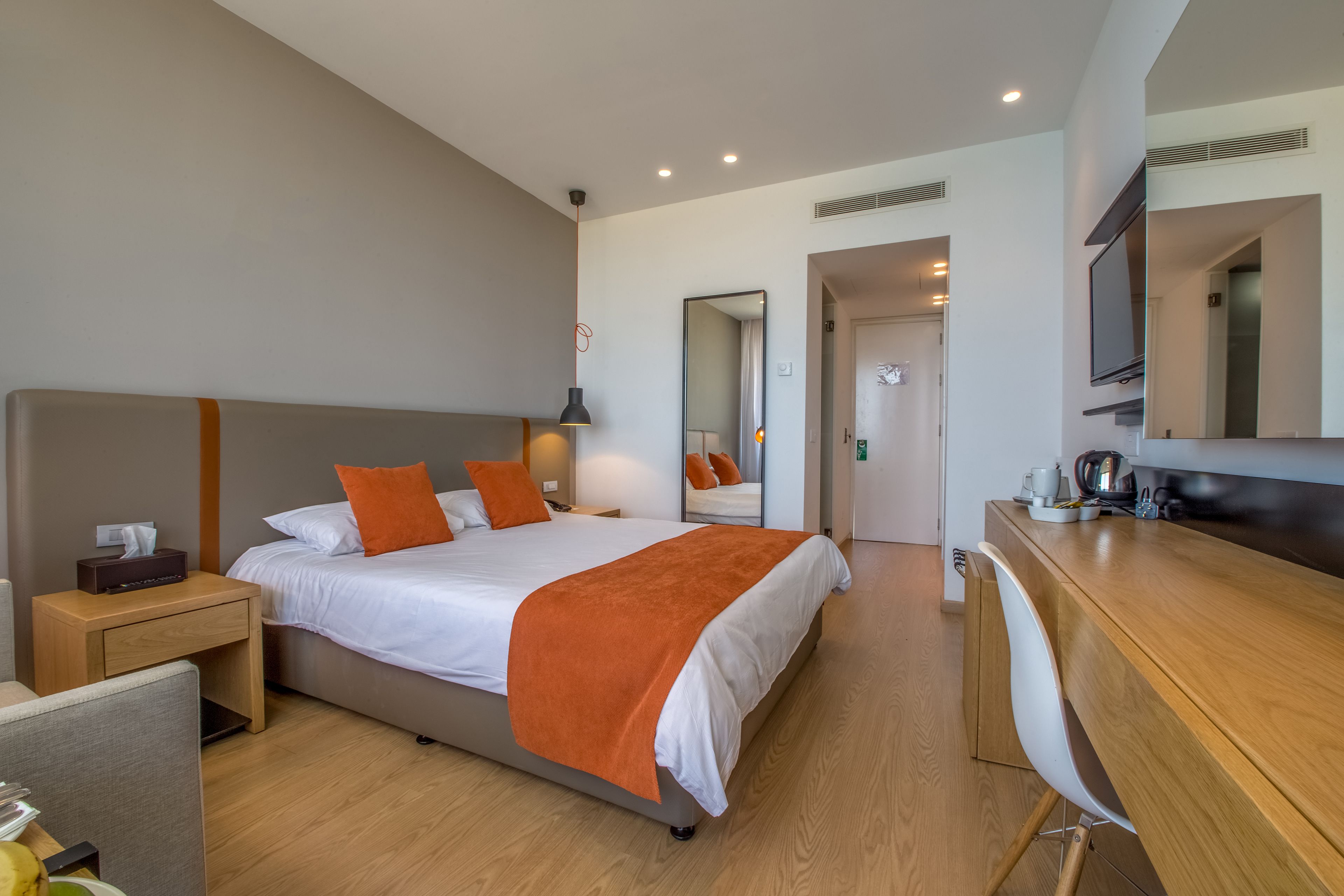 A modern hotel room with a large bed, a desk, and a mirror.