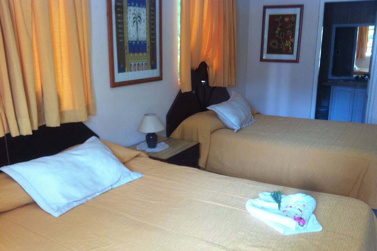 Ein Hotelzimmer mit zwei Betten, einem Nachttisch, einer Lampe und einem gerahmten Bild an der Wand.