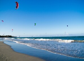 Ein Strand mit Wellen und mehreren Drachen am Himmel.