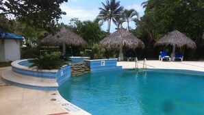 A swimming pool with a blue tiled edge, surrounded by palm trees and thatched umbrellas. - Beach House Cabarete by Faranda Hotels (Cabarete)