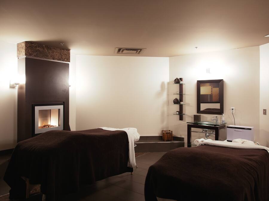 A room with two beds, a small table with a mirror, a shelf with toiletries, and a wall-mounted heater.