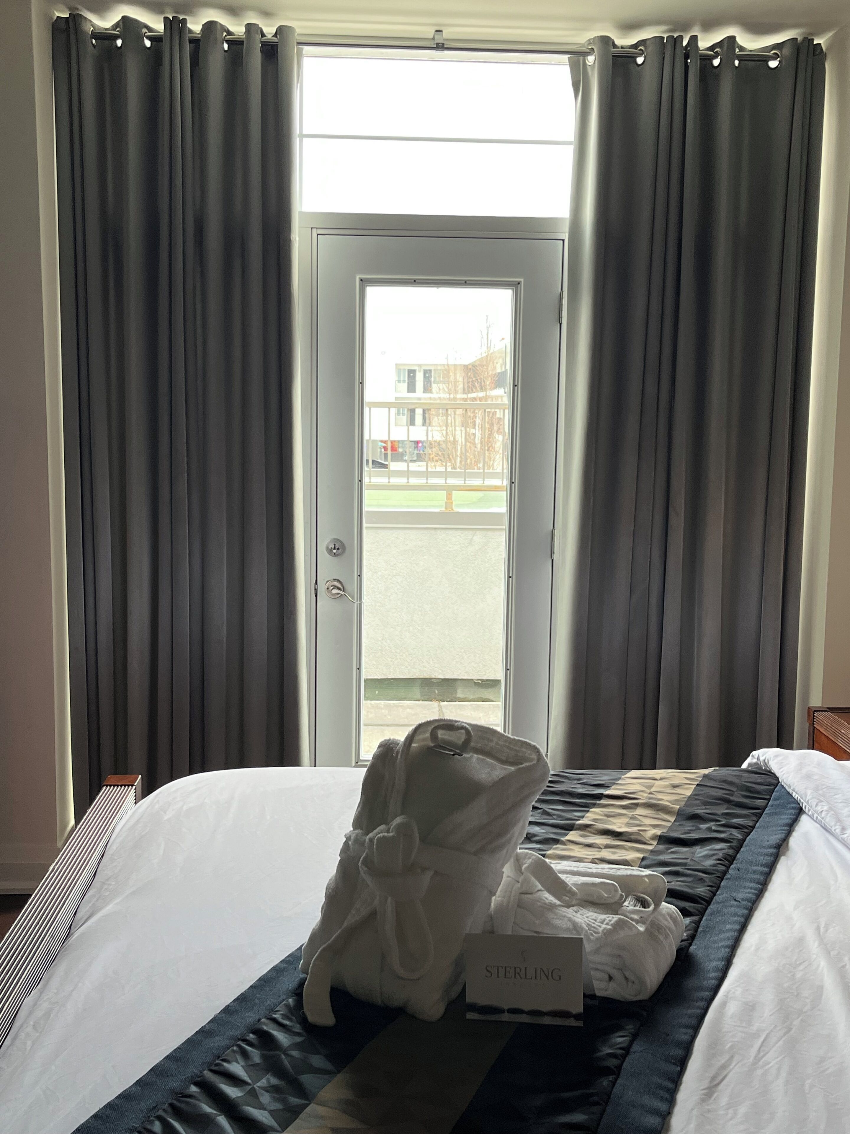 A hotel room with a bed, a set of towels, and a view through a door.
