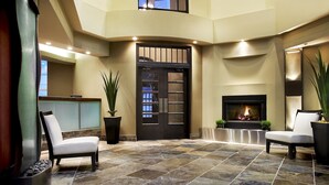 A lobby with a stone floor, two white chairs, a reception desk, a black door, and a fireplace.