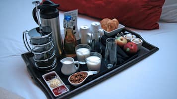 Ein Frühstückswagen mit Kaffee, Milch, Croissants, Äpfeln und Beilagen auf einem Bett.