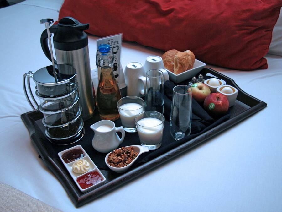 Ein Frühstückswagen mit Kaffee, Milch, Croissants, Äpfeln und Beilagen auf einem Bett.