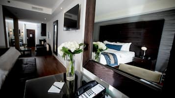 Habitación de hotel con cama, escritorio con teléfono, florero con flores y televisión montada en la pared.