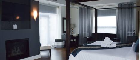 A modern hotel room with a large bed, a fireplace, a desk, and a television.