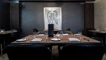 A dining area with a long table set for four, a modern abstract art piece on the wall, and dark wood paneling.