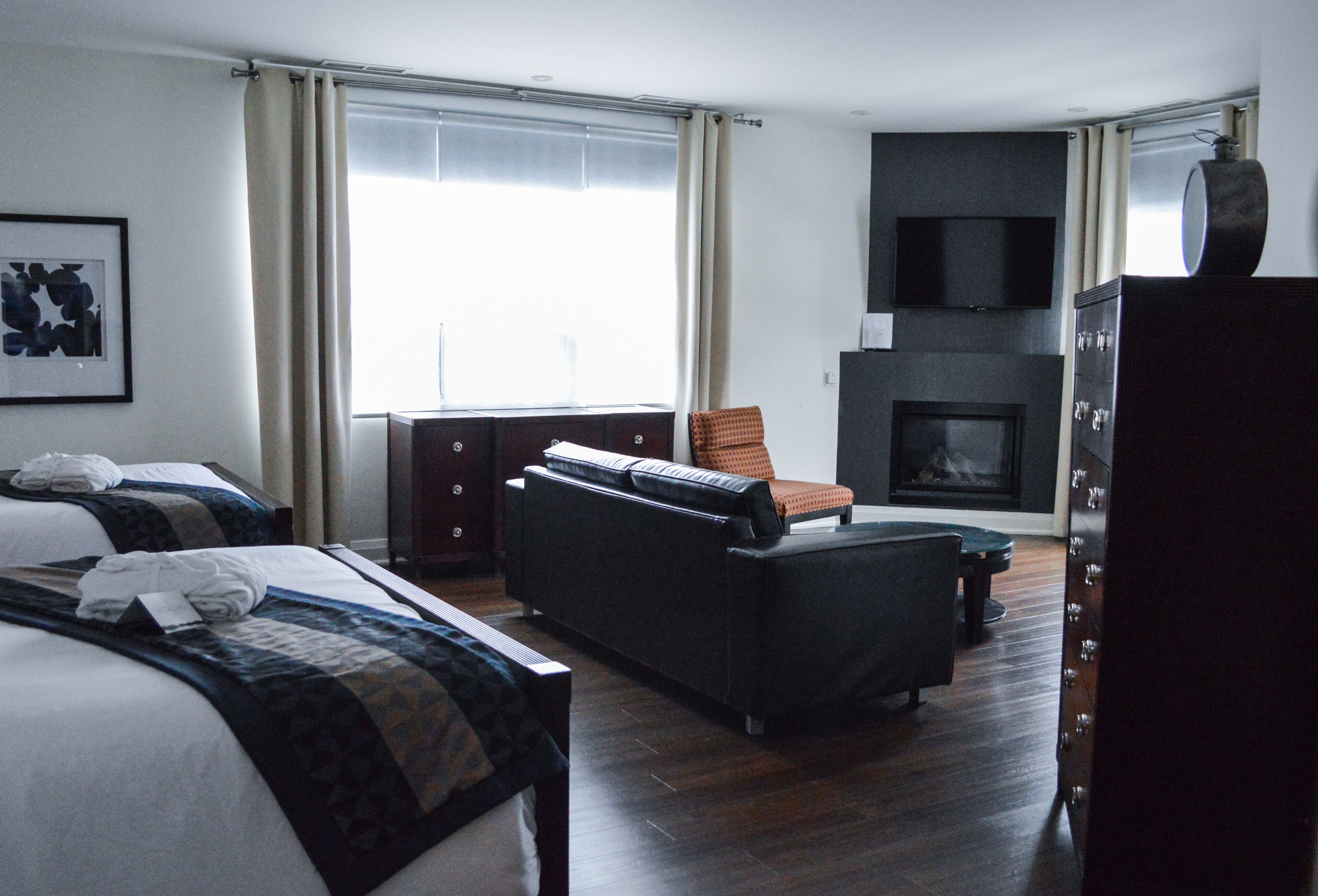 Ein Hotelzimmer mit zwei Betten, einem Schlafsofa, einem Fernseher, einem Kamin und einem großen Fenster mit Vorhängen.