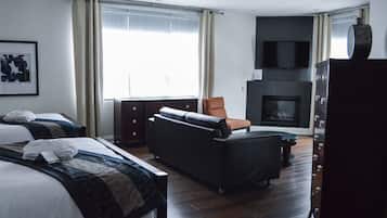 Ein Hotelzimmer mit zwei Betten, einem Schlafsofa, einem Fernseher, einem Kamin und einem großen Fenster mit Vorhängen.