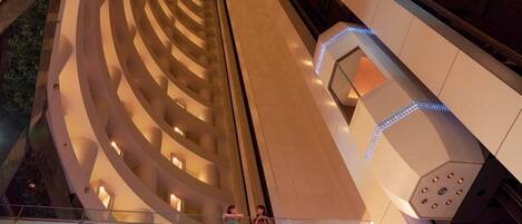 A modern hotel interior with a central spiral staircase, multiple balconies, and a glass railing.
