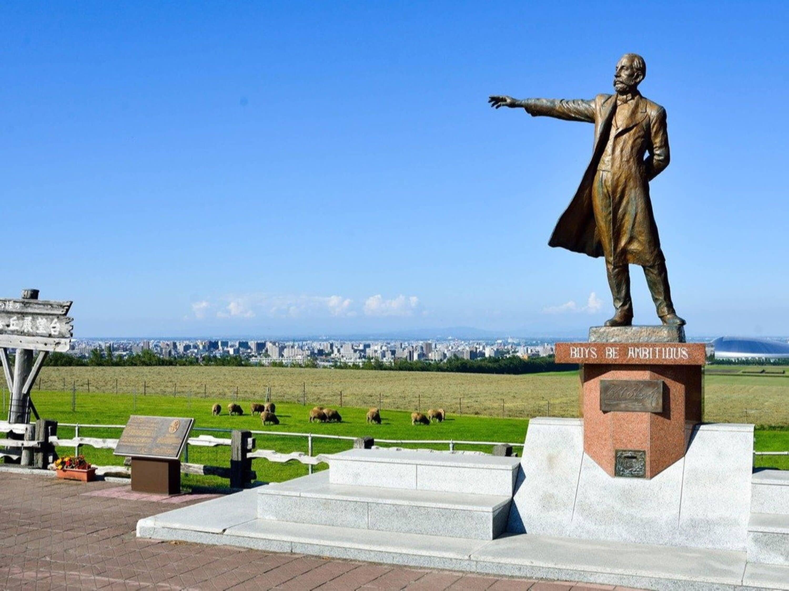 A statue of a man with outstretched arms on a pedestal, with a cityscape in the background.