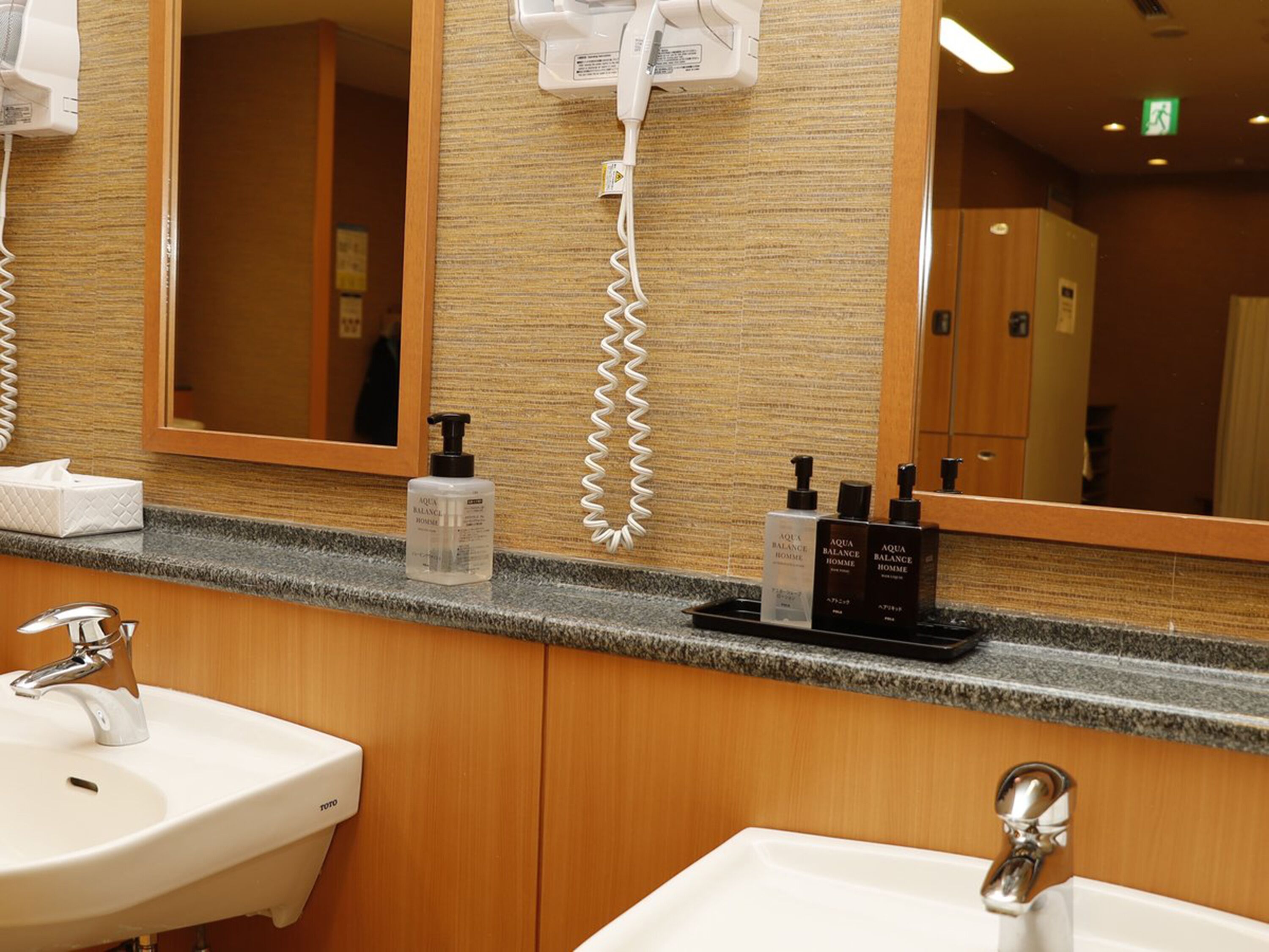 A hotel bathroom with two sinks, a large mirror, a hairdryer, and toiletries on the counter.