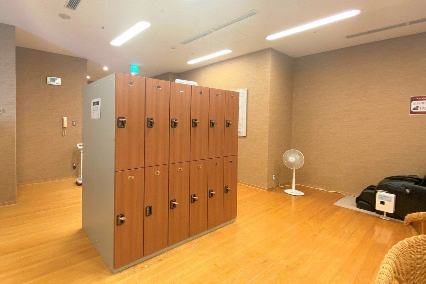 A hotel room with wooden lockers, a scale, a fan, and a charging station.