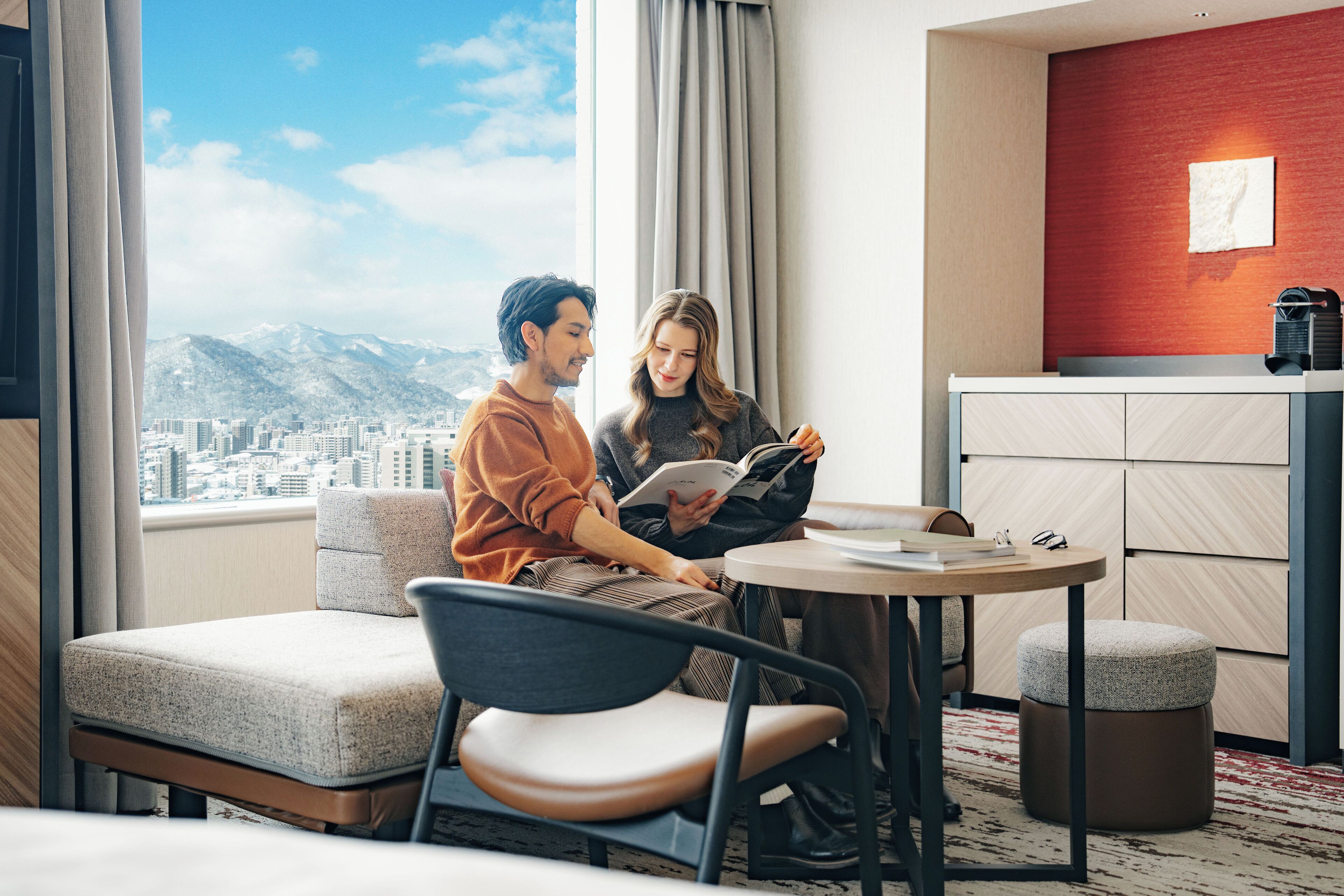 Una habitación de hotel moderna con vistas a la ciudad, una mesa redonda, un sofá y una pequeña kitchenette.