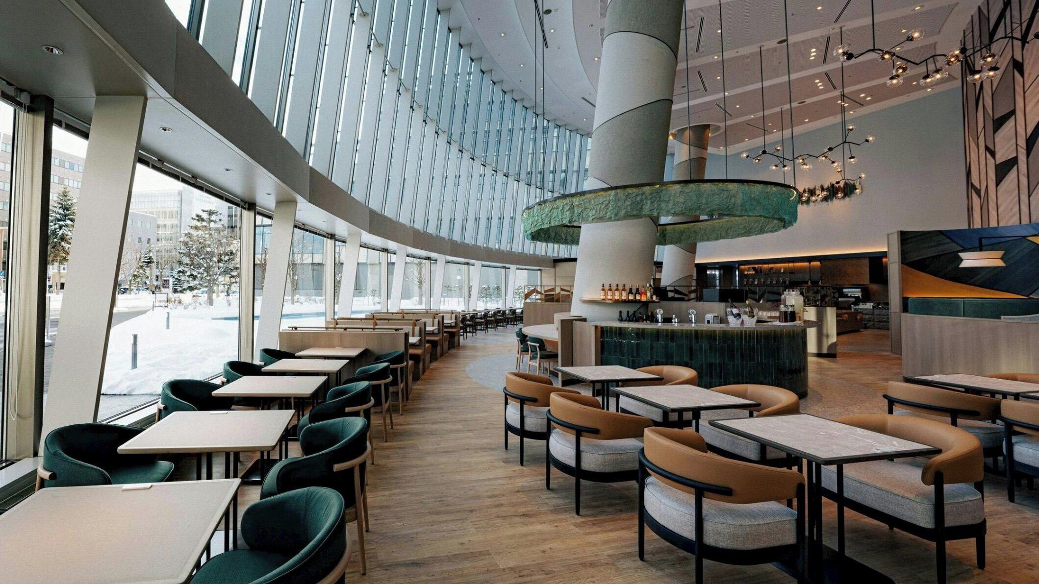 A modern restaurant with a high ceiling, large windows, and a central bar area.