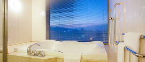 A modern bathroom with a large bathtub, a shower with a glass door, and a window with blinds.